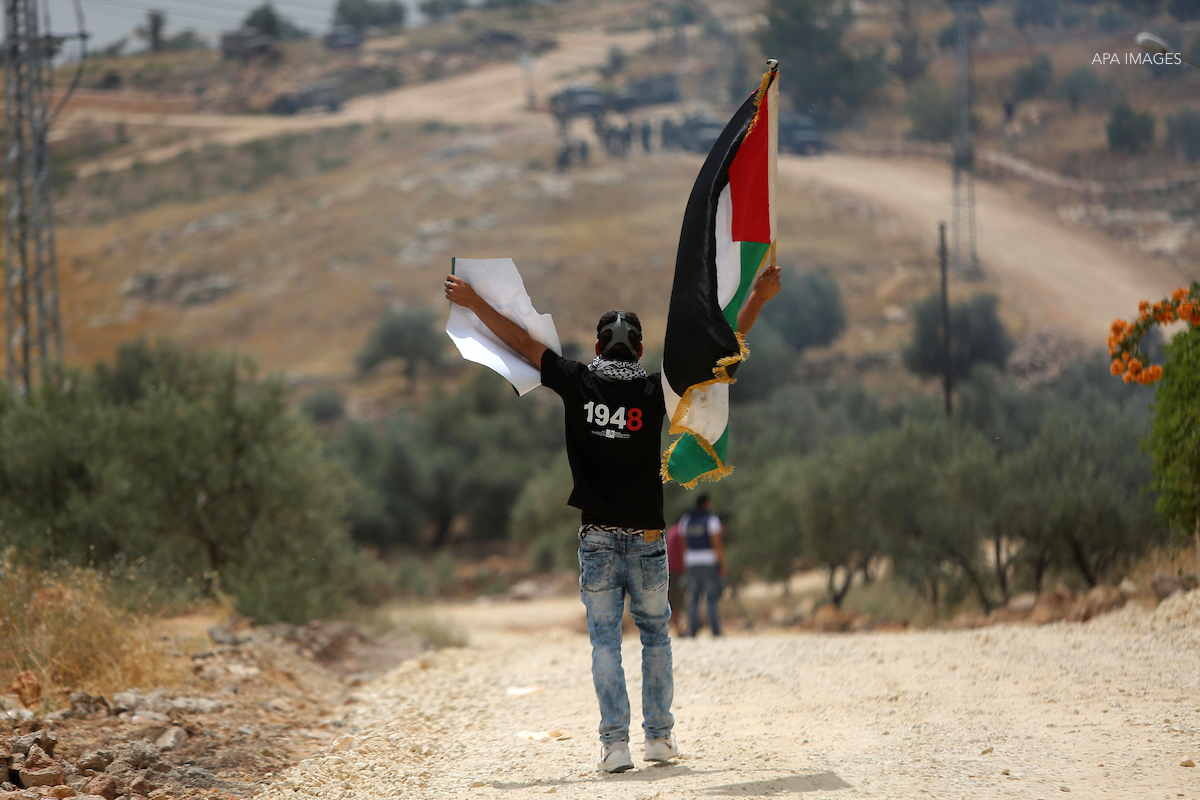 A Palestinian protester holds a Palestinian flag during clashes with Israeli troops at a protest ahead of Nakba day